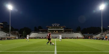 College soccer player dribbling ball under bright stadium lights, representing future MLS talent.