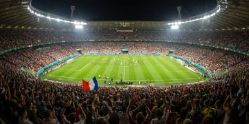 Vibrant soccer stadium filled with enthusiastic fans under bright lights during a night match.