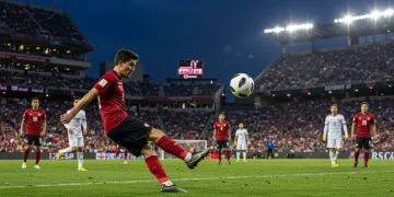 Soccer player striking a powerful free kick towards goal in a US soccer stadium.
